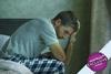 Man sat on bed holding his head in his hand