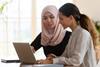 Two women on different races sat together at a laptop