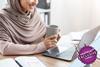 Woman sat at laptop holding a coffee