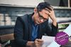 Man sat at desk reading paperwork with his head in his hand