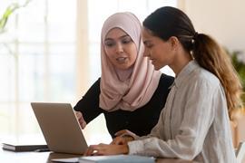 Two women on different races sat together at a laptop