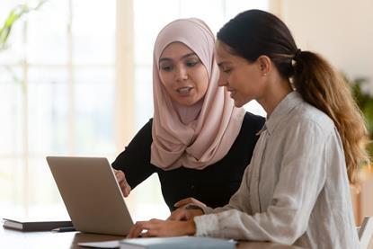 Two women on different races sat together at a laptop