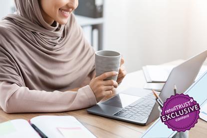 Woman sat at laptop holding a coffee