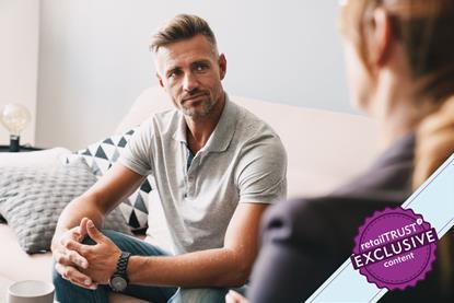man sat on sofa with hands clasped listening to a friend