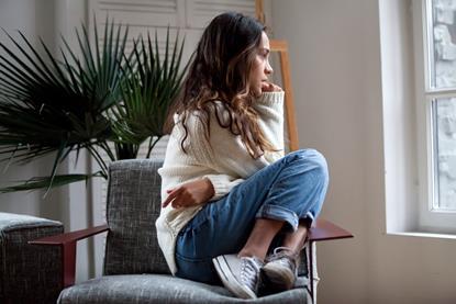 woman curled up on a chair biting her nails staring out of a window